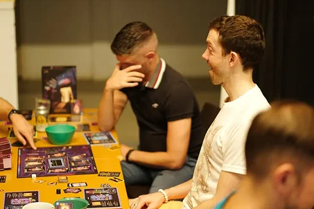 Vrienden die samen aan tafel een bordspel spelen en enthousiast reageren tijdens het spel.