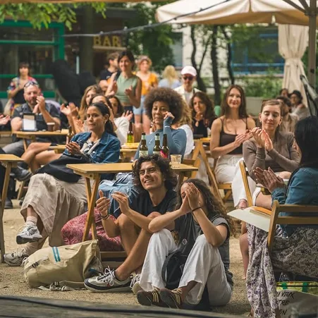 Een groep mensen die buiten op een terras zit en applaudisseert tijdens een gezellige bijeenkomst in een caféomgeving.